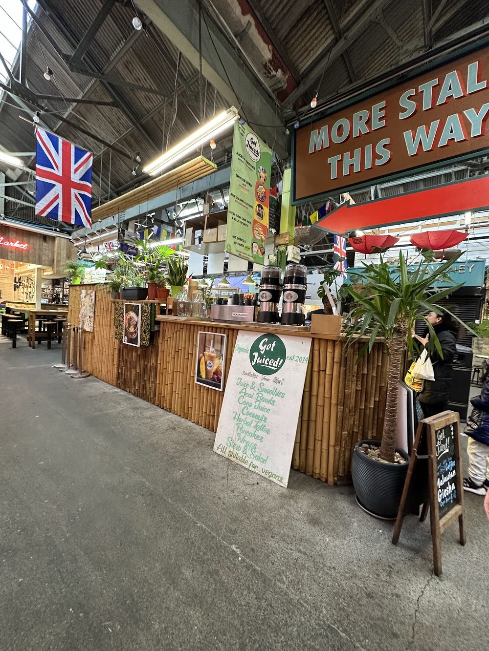 The Juice Hub & Co stall seen down the aisle of Tooting Market, plants and blender bottles along the bamboo front